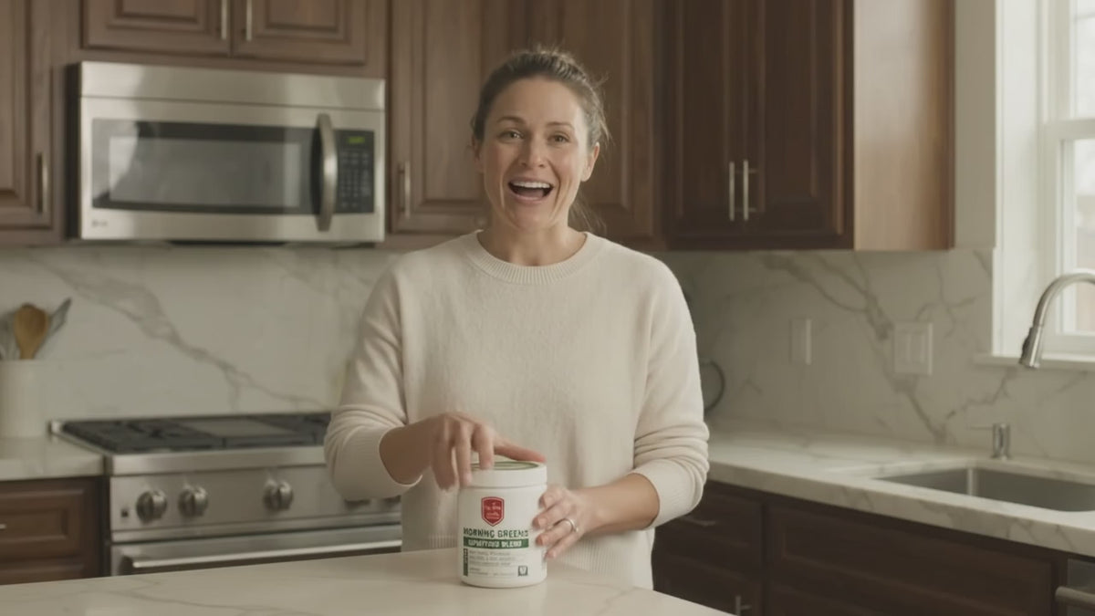 Woman mixing a scoop of Drs Diet Morning Greens Superfood Blend into a glass of water in her kitchen