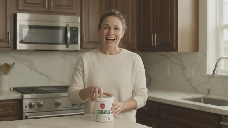 Woman mixing a scoop of Drs Diet Morning Greens Superfood Blend into a glass of water in her kitchen